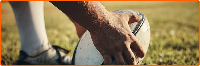 Rugby player gripping a ball tightly on a sunlit field before play, highlighting strength, control, and tactical preparation during a competitive match.